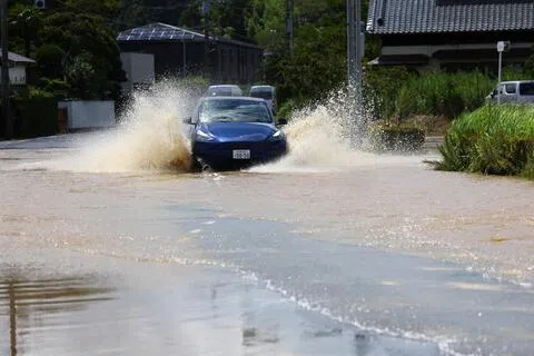 图为8月14日，日本千叶县大网白里市，一辆汽车在积水的道路上行驶。（路透社）