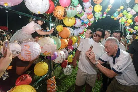 德义中秋节游园会星期六在碧山—宏茂桥公园举行，现场的精美布置营造了浓浓的中秋氛围。图中是人协百盛艺术社区的艺术装置“我们的邻里瑰宝”，由居民在纸灯笼上绘制宏茂桥地标，连接成一条璀璨闪耀的灯笼隧道。负责德义区基层事务的国务资政李显龙（右）忍不住多拍一些照片。（李冠卫摄）