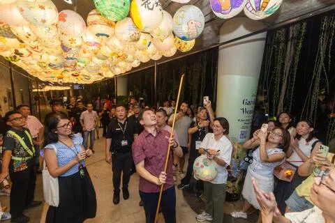 也是华社联络组主席的国家发展部长徐芳达（中）在擎天树丛附近的“灯廊”，挂上自己画的灯笼。（吴先邦摄）