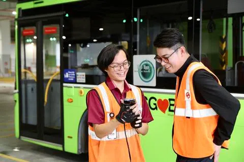 王杰瑞（左）刚在去年10月加入SMRT，是最年轻的新加坡籍车长。他向巴士服务控制员张伟俊展示车长管理系统应用，系统显示他驾驶表现良好，可在安全驾驶奖励计划下以分数兑换购物券。（陈斌勤摄）