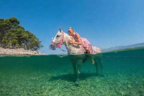 席卷欧洲的热浪逐渐往东转移，克罗地亚著名旅游景点布拉奇岛上，一名女游人骑着马泡在海水中。（路透社）