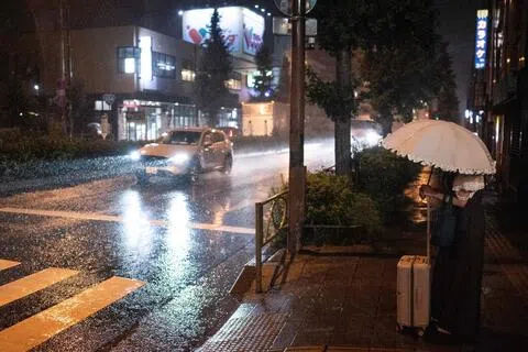 受气候变化影响，东京从8月27日至10月2日连续降雨37天，创下了自1886年有可比数据记录以来的最长连续降雨纪录。图为9月6日，一名女子在东京街头等待过马路。（法新社）