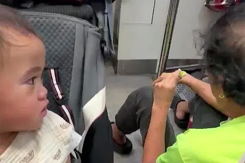 身穿绿色上衣背对镜头的男子（右）在地铁车厢内席地而坐吃着包子，再把咬过的包子递到男童卡里斯（左）嘴边，几乎碰到孩子的嘴唇，令家长大为震惊。（受访者提供）