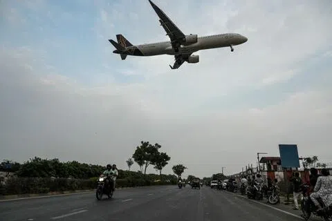 People travel along a road as an Air India Vistara aircraft prepares to land in Ahmedabad on September 5, 2026. (Photo by Shammi MEHRA / AFP)（AFP）