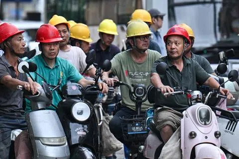 中国中小微企业按最低基数而非实际月薪为员工社保缴费、节省开支的现象普遍存在。图为一群建筑工人星期四（8月13日）骑着电动自行车下班，在上海一处路口等待过马路。（法新社）