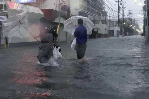 日本千叶县市川市灾情严重，一处街道严重积水，人们只能卷起裤脚涉水而过。（路透社）