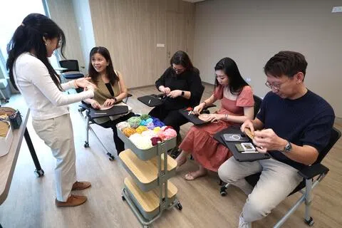 触爱辅导与心理服务部社工陈佳敏（左一），邀请触爱坊@资金大厦启幕仪式的访客，通过编织毛线纾解心理压力。（陈斌勤摄）
