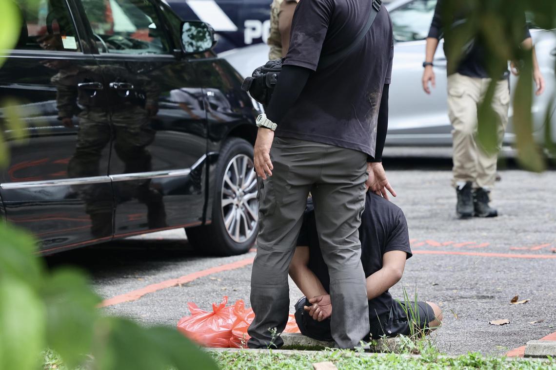 一名嫌犯双手上铐,坐在露天停车场的路缘等待警员进一步指示。(陈斌勤摄)