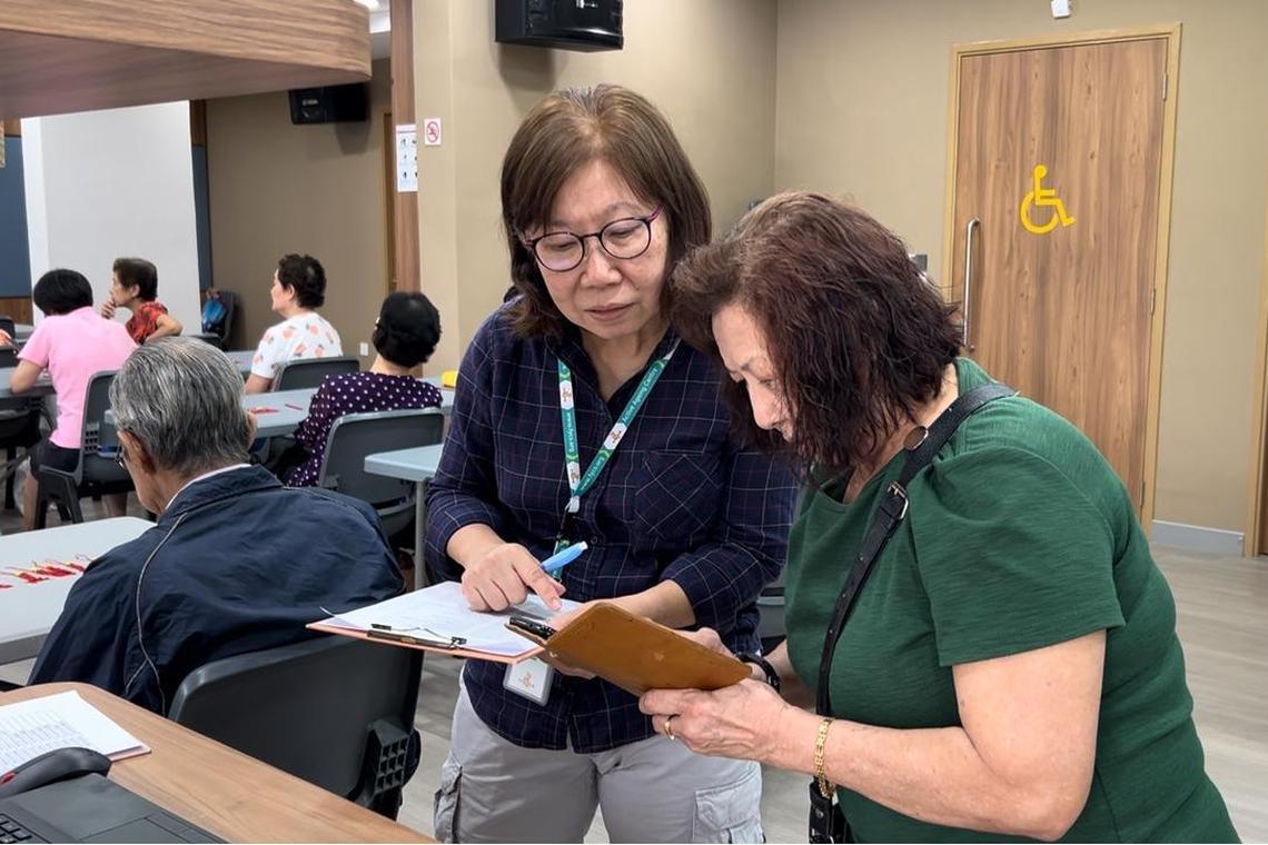 飞跃活跃乐龄中心义工兼会员郑美珍(左),教导会员用手机扫描签到参加手工班。(受访者提供)