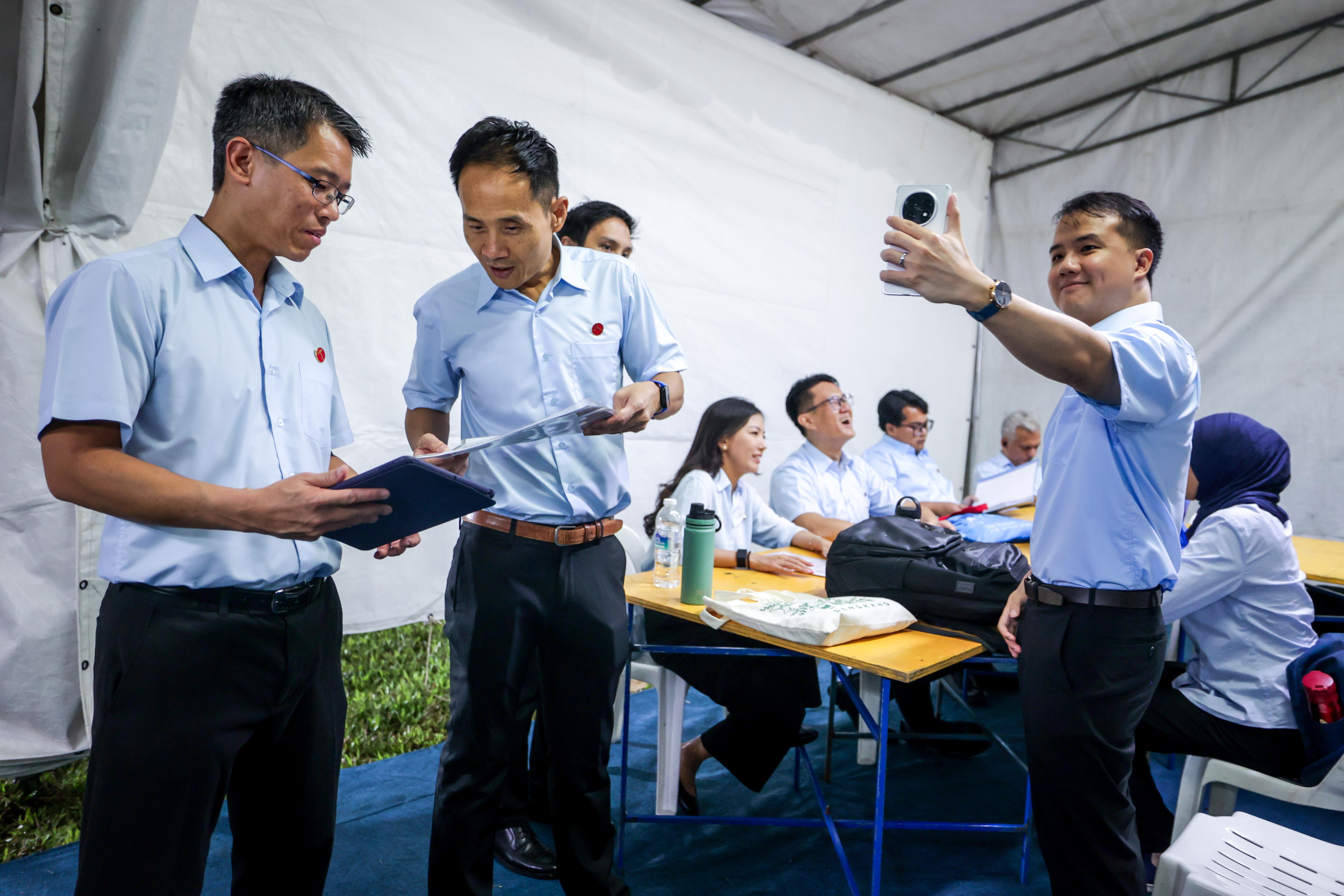 工人党4月24日在盛港安谷弯The Vales公寓旁的草场举行群众大会。活动开始迎接沸腾群众之前,候选人在后台贮备就绪,严燕松(左起)和符策涫在讨论演讲稿,而刘宇扬则拿起手机自拍,捕捉团队的幕后花絮。(叶振忠摄)