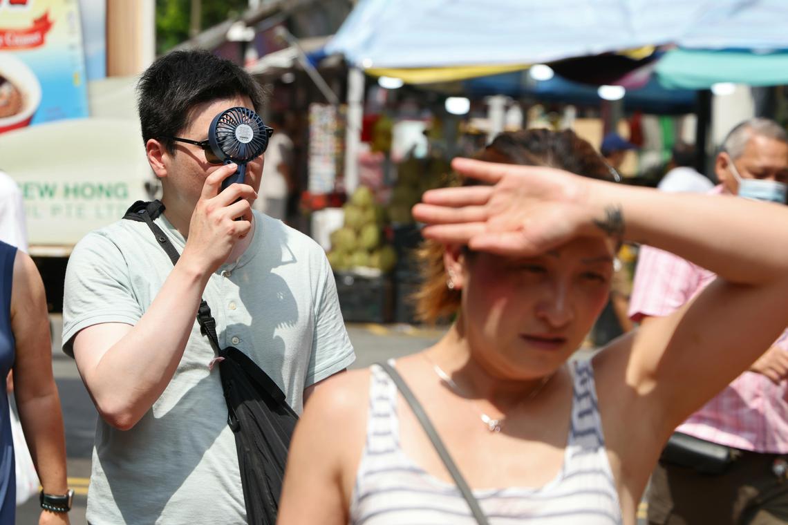 牛车水街道上呈现一副炎阳高照的景象,大批游客都打起了遮阳伞,有些行人还自带小风扇来降温。(梁麒麟摄)