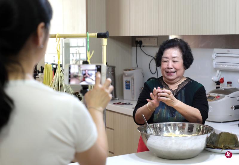 晋江会馆会员陈玉叶熟练地包粽子，女儿在旁摄制两分钟视频，准备提交参加“疫见粽情”端午线上文娱晚会的包粽子比赛。（林国明摄）