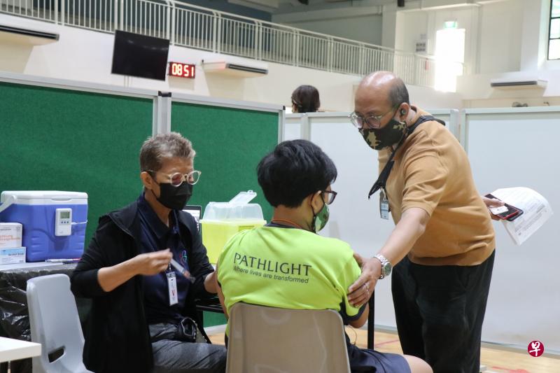 约120名新光学校学生昨天回校接种冠病疫苗，学生可由一名家长陪伴。图中这名父亲在孩子准备打针时，轻轻握住孩子的手臂，给予鼓励。（新光学校提供）