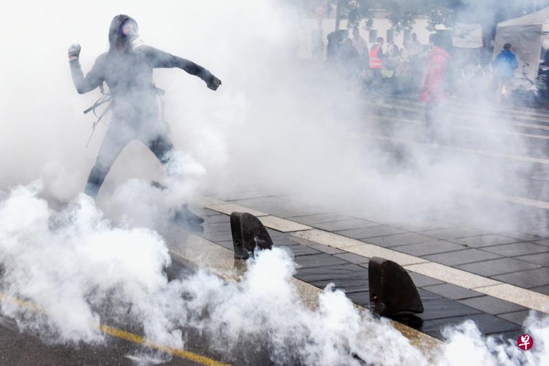 法国西部城市南特周六爆发警民冲突，警方向反对健康通行证计划的示威者发射催泪弹，一名戴着防毒面罩的示威者将催泪弹瓦斯罐向执法人员丢回去。（法新社）