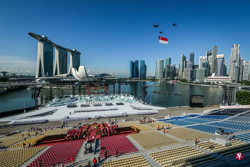 国庆检阅礼昨天上午在滨海湾浮动舞台举行，图为直升机吊挂巨型国旗飞越会场上空，为国家庆生的一刻。因疫情关系，今年检阅礼的步操队伍受限，看台上也只邀请100名嘉宾观礼。（叶振忠摄）
