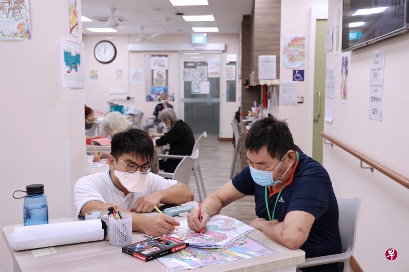 去年中风的李文生（右）每天由专车将他带到万国康乐轩，除了进行复健，他也能参与其他运动和艺术活动，以及与其他年长者聊天。中心看护张伟麟（左）就经常陪着他作画和聊天，如今的他精神奕奕，并且已经能独立行走。（梁麒麟摄）