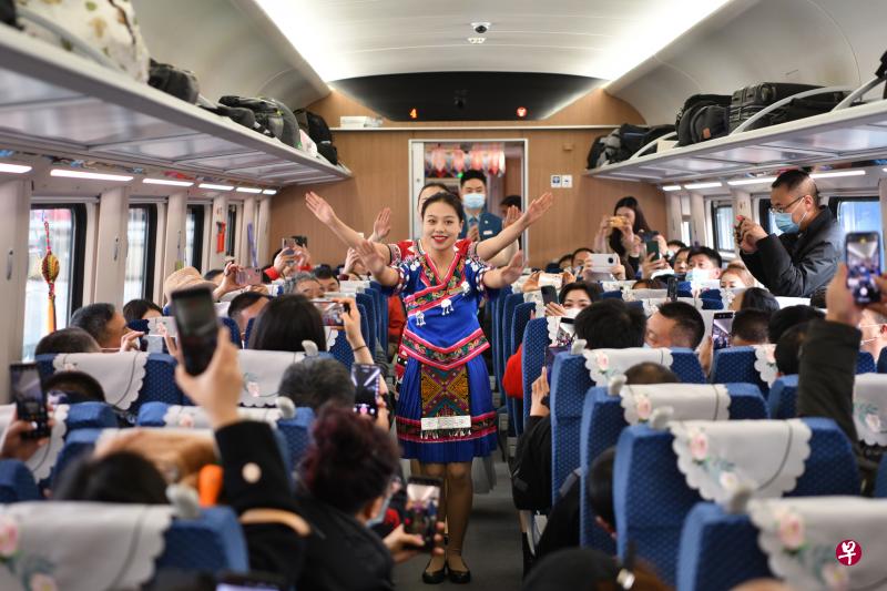 载着700多名乘客的C3次动车复兴号，昨天下午4时45分，缓缓驶出昆明火车站，标志着中老铁路全线开通运营，老挝自此迈入铁路运输时代。图为身着民族服饰的中国列车员为旅客带来民族特色节目。（中新社）