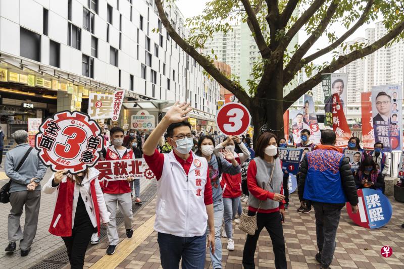 香港工联会会长吴秋北（举手者）昨天在香港立法会选举投票日恳请市民投自己一票时，与民建联新星梁熙的支持者狭路相逢，礼貌性挥手致意。（彭博社）