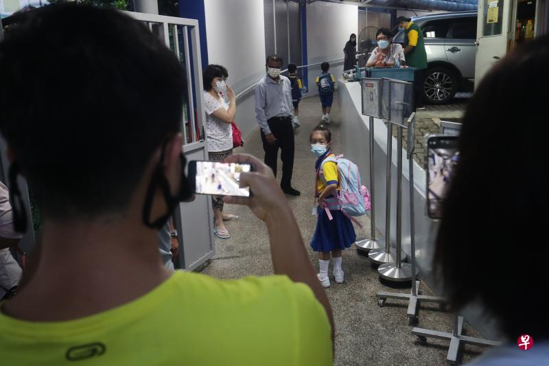 锦明小学不允许家长陪孩子报到，只在休息时间让家长入校观察。图中这名家长目送女儿踏进校园，拍照记录她开启小学生涯的时刻。（蔡家增摄）