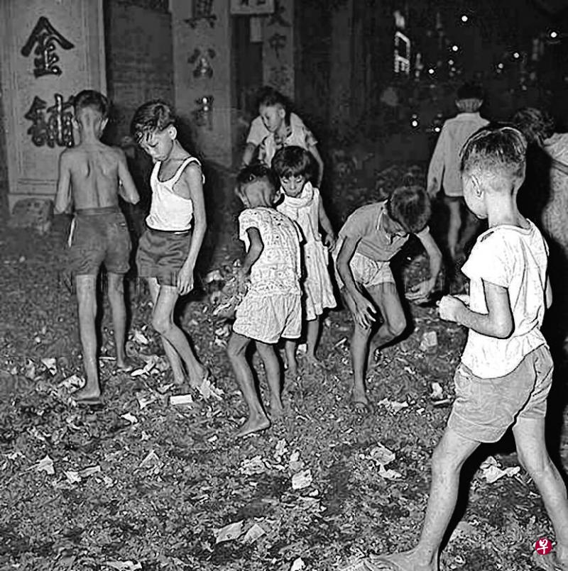 除夕夜大坡大马路的恒利金铺燃放长爆竹后，小孩在满地红彤彤的纸屑中寻宝。