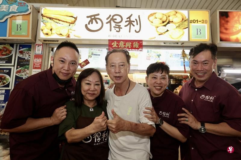 百年老字号西得利的第三代摊主许振西（中）、太太翁素贞（左二）、大儿子许环杰（右起）、女儿许美玲，以及小儿子许珉铨（左一）在金文泰的摊位前合照。（邬福梁摄）