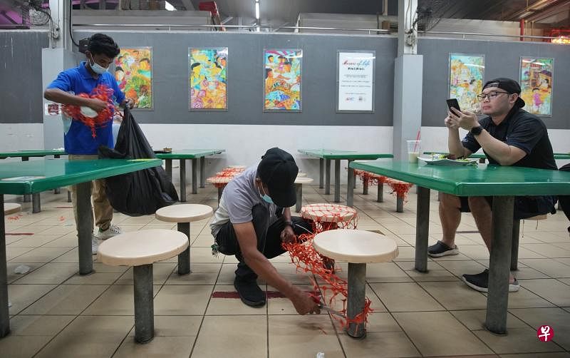配合安全管理措施放宽，多个小贩中心和咖啡店昨天派人拆除围网和桌椅的贴纸。（谢智扬摄）
