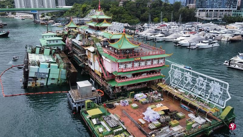 香港珍宝海鲜舫旁的厨房船（左）前天深夜倾侧入水，船身近乎90度塌下，躺卧水上，被警消人员以红色浮带围起来。（中通社）