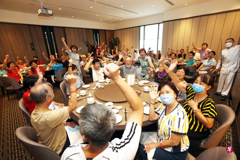 四川豆花饭庄行政董事黄玮玲（左边站立者）以及中区市长潘丽萍（中间站立者），与年长者在活动现场互动，欢唱《月亮代表我的心》。（邝启聪摄）