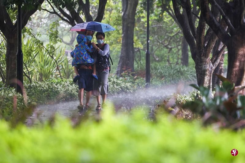 爸爸抱着小孩，与妈妈在雨中撑伞同行，画面让人安心。（白艳琳摄）