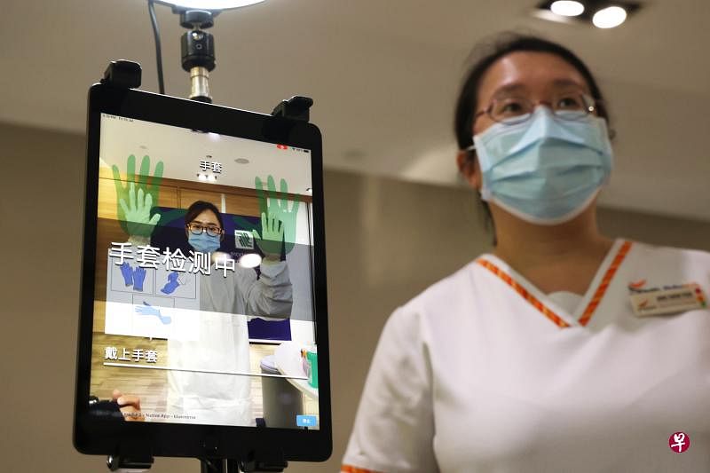 新加坡中央医院的医护人员和访客日后可使用新推出的智能系统，按照“智能镜子”显示的防护装备穿戴流程和语音指示，学习如何正确穿戴个人防护装备。中央医院护理品质研究与转型单位护理副处长洪欣玉（右一）星期五向媒体介绍智能系统的使用方法。（邝启聪摄）