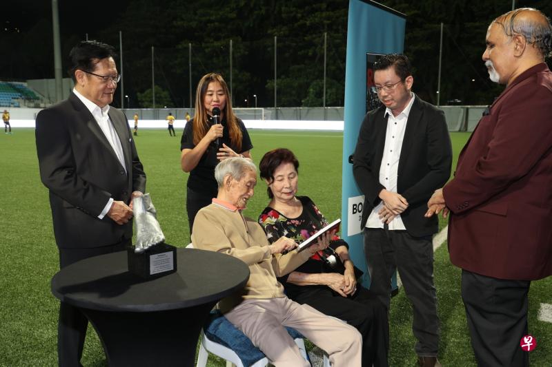▲谢文龙（坐者左）和妻子阅读新书，左为新加坡足总会长林家栋，右起为新书作者拉朱和编辑许来福。（蔡家增摄）