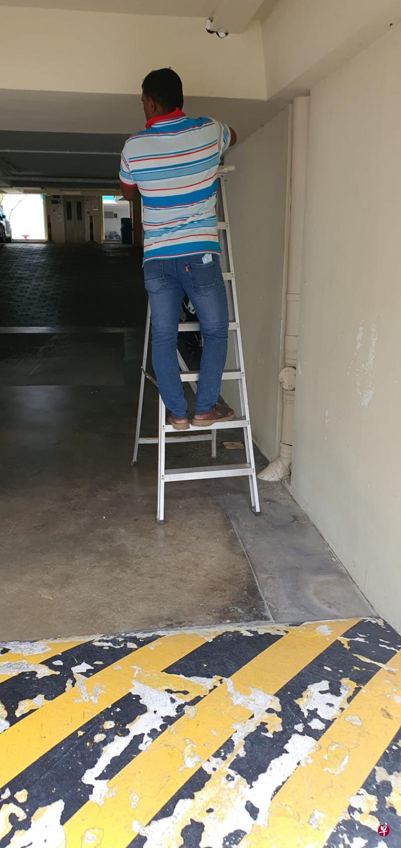工人在昏暗的停车场内工作时没穿反光外套，穿着拖鞋就爬上梯子。（作者提供）