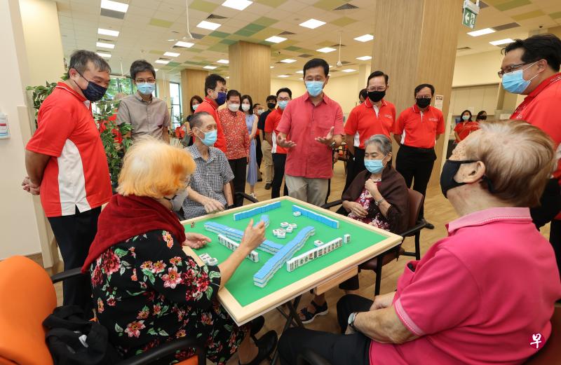 卫生部长王乙康（中）在广惠肇留医院主席李国基（站立者，右三）的陪同下参观广惠肇位于波东巴西1道的分院。这家疗养院也设有活跃乐龄中心，为居民举办麻将等康乐节目，让年长者保持身心活跃。出席活动者包括波东巴西区议员司徒宇斌（站立者，左一）。（唐家鸿摄）