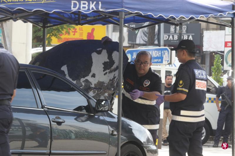 警方鉴证组人员仔细搜查死者的汽车，汽车引擎盖上明显可见被爆炸物损毁的痕迹。（东方日报）