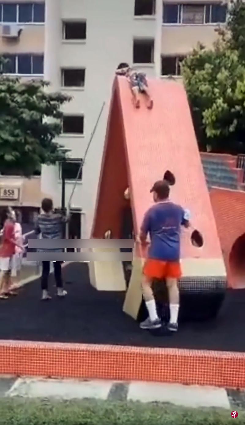 幼童爬上约45度的攀岩墙后进退不得，需要旁人协助将他救下来。（视频截图）