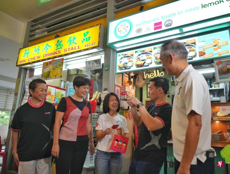 星展银行接下来一年，将给予使用PayLah!应用支付餐食费的公众最多3元的即时回扣。总理公署部长兼财政部及国家发展部第二部长英兰妮（左二）和星展银行新加坡总监兼董事总经理许志坤（右二）在中峇鲁熟食中心向公众和摊贩介绍这项计划。（谢智扬摄）