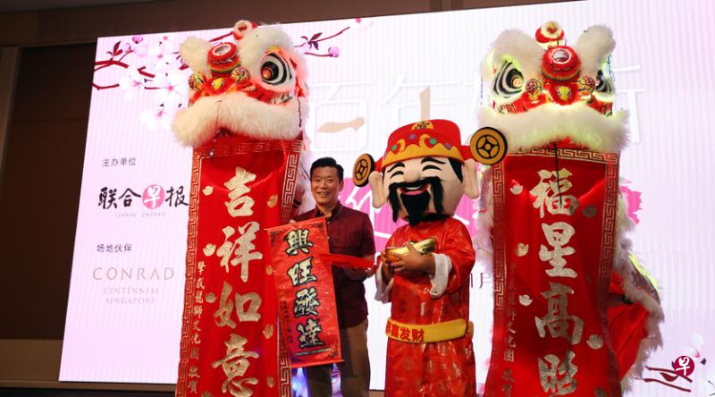 《联合早报》总编辑吴新迪从舞狮和财神手中接过吉祥春联。