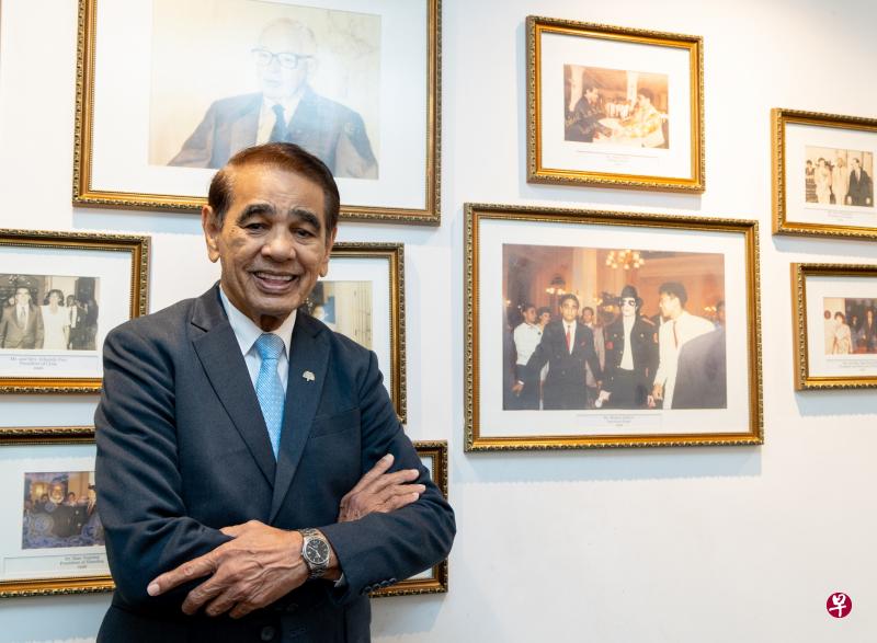 84岁的雷斯利·丹克已在莱佛士酒店工作长达51年，接待过的贵宾不计其数。他说，只要身体状况许可和酒店愿意聘请他，就会继续做下去。墙上照片为美国已故巨星麦克杰逊（中）访新时，雷斯利·丹克（照片第一排左）负责接待。（张思庆摄）