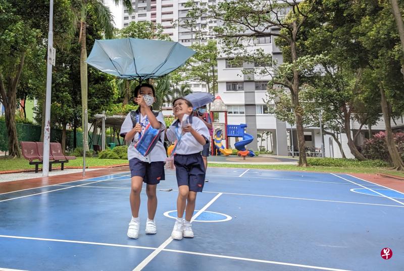 全岛一连两天下起长命雨，两名小学生共撑一把伞，大风把雨伞吹得往上翻，让他们忍不住笑了起来。（李冠卫摄）
