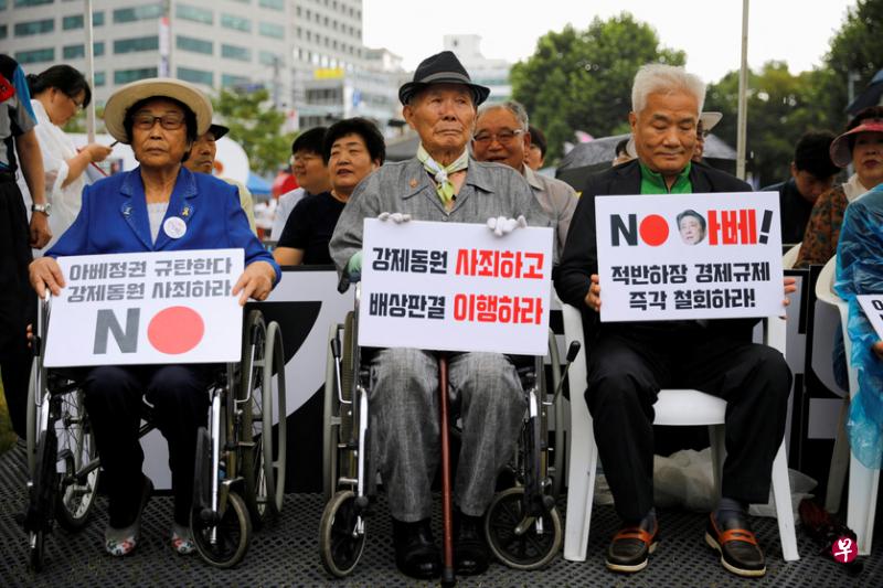日本殖民时期被强迫劳动的受害人在首尔举行的光复节反日抗议活动中，高举要求日本“为强迫劳动致歉和履行赔偿”的标语牌。（路透社）
