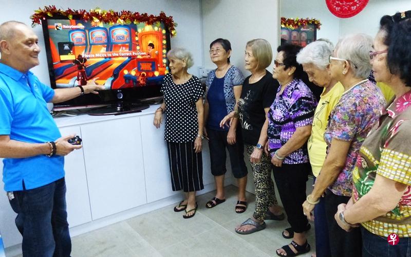 蔡锦基（左一）在“狮子乐龄之友协会”的文礼支部当义工，筹备康乐活动，包括教该区年长者玩Xbox Kinect。
