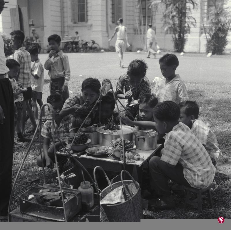 上世纪60年代，街边小贩挑担卖沙爹，一群男生吃得不亦乐乎。（档案照）
