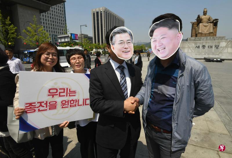 支持南北和解的韩国民众昨天在首尔光化门广场集会，两名参与者分别戴上文在寅和金正恩的面具，旁边的字幅上写着“我们要结束战争”。（法新社）
