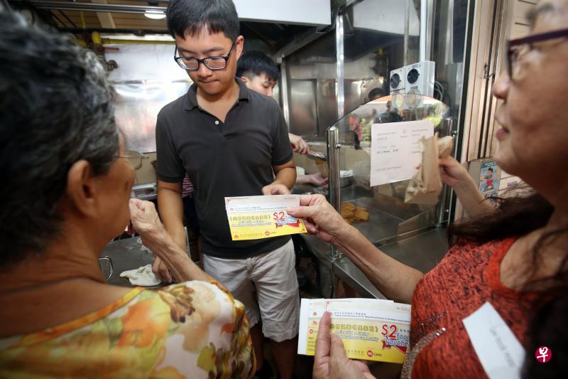 新加坡全国商联总会为全岛1500名贫困居民派发30元餐券。裕廊居民郭五妹（右）昨天替因病无法工作的丈夫领取固本后，用餐券到小贩中心为他买早餐。（邝启聪摄）