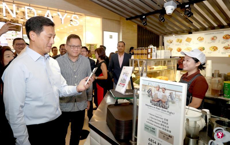 教育部长、金管局董事王乙康（左起）在面包物语区域总经理林青材陪同下，在土司工坊扫描SGQR码买咖啡。（周国威摄）