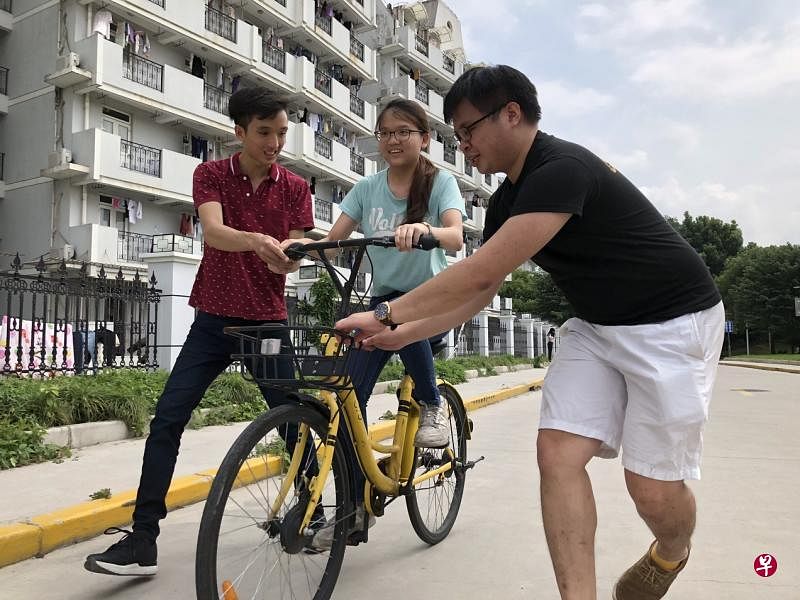 学长俊颖（左）和凯杰（右）努力地扶着靖雯（中间）掌握骑车平衡。（林敬翔摄）