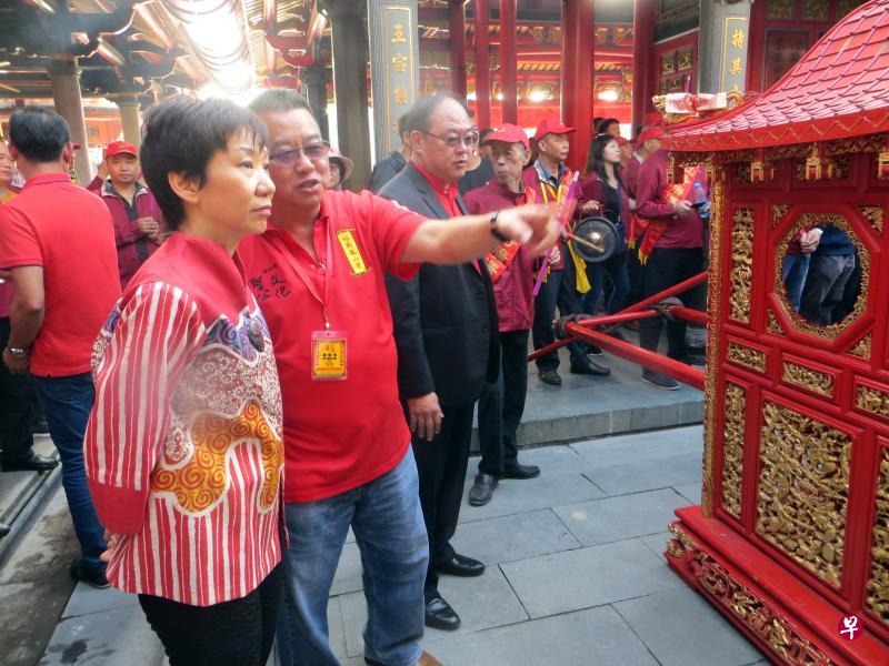 傅海燕在南安诗山凤山寺参观迎神下山巡按赐福的民间活动。正在向她讲解的是圣公文化传承委员会秘书长林清河。穿大衣者为新加坡宗乡总会会长、圣公文化传承委员会顾问陈奕福。（谢燕燕摄）