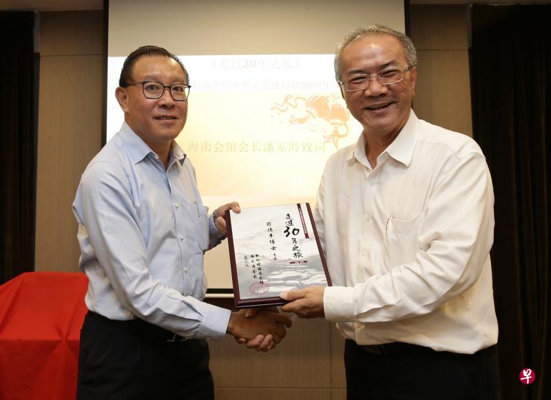 新加坡海南会馆会长潘家海（右）赠送《走过30年之旅》纪念刊给为中华文史课程服务了30年的符传丰讲师。（陈渊庄摄）