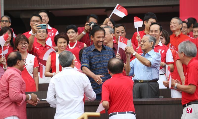 马来西亚首相马哈迪（浅蓝衣者）与文莱苏丹波基亚（深蓝衣者）在国庆庆典现场，与我国多名部长与议员打招呼，气氛友好。（谢智扬摄）