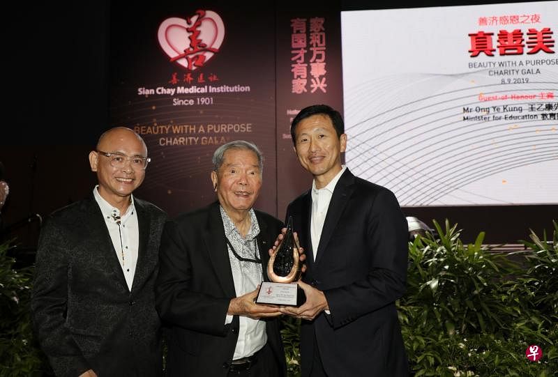 教育部长王乙康走下讲台，将善济“特别贡献奖”奖座颁给94岁的新加坡鳄鱼牌公司创办人陈贤进博士（中）。左为善济主席卓顺发。（林国明摄）